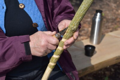 Nærbillede af hånd der snitter en lang spiral på en pind